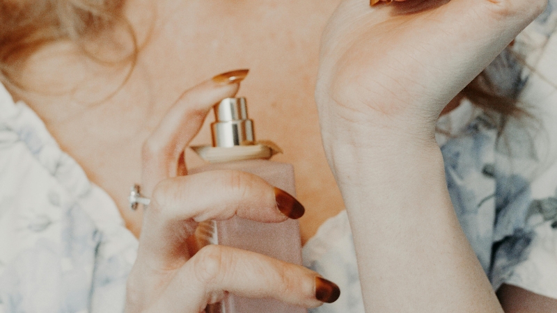 A woman spraying perfume on her wrist from a light pink bottle