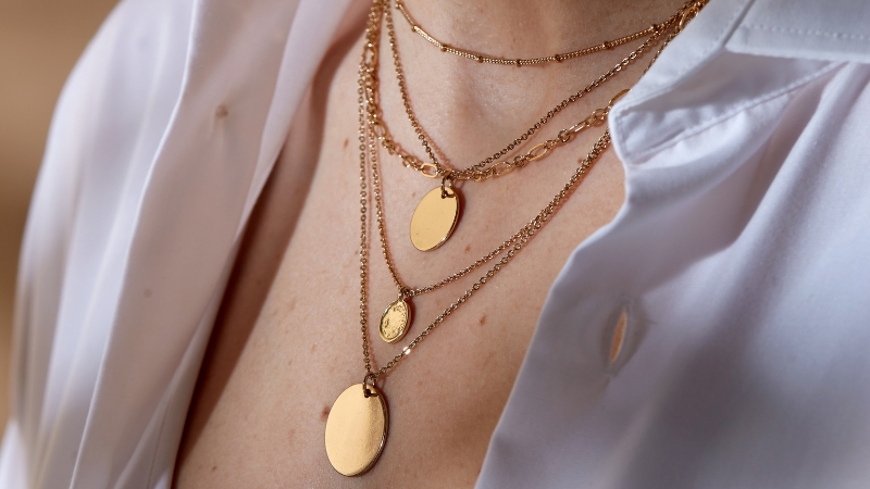 Layered gold necklaces with round pendants styled over a white blouse as affordable jewelry that looks luxe