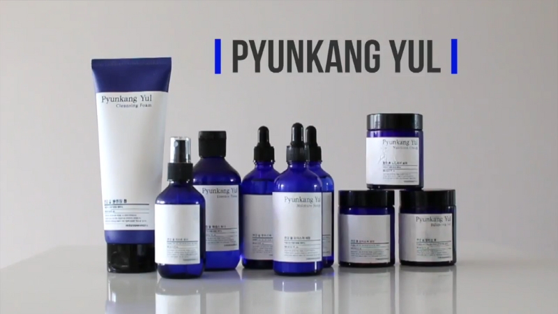 A collection of Pyunkang Yul skincare products in blue bottles and jars is displayed on a white surface