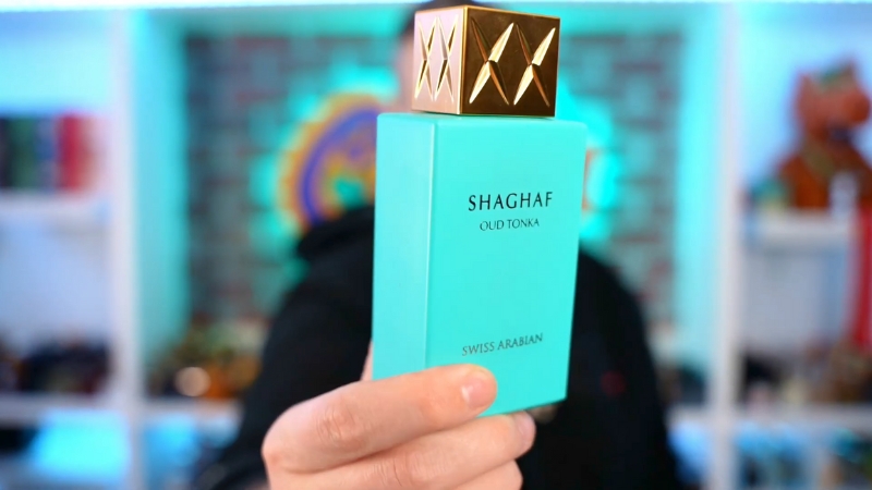 A hand holding a turquoise bottle of Swiss Arabian Shaghaf Oud Tonka with a gold cap
