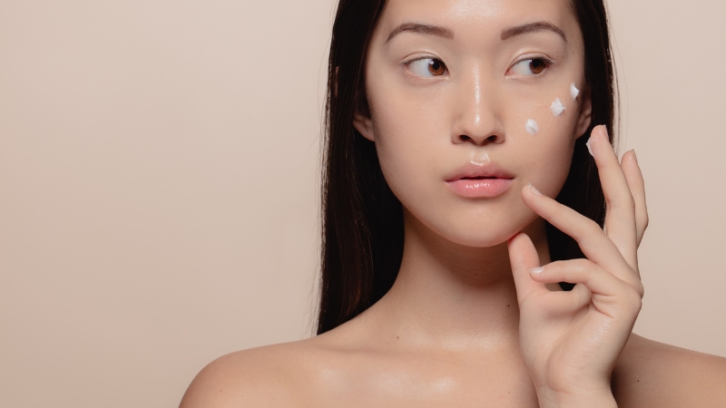 A young woman applies a vegan Korean skincare cream to her cheek