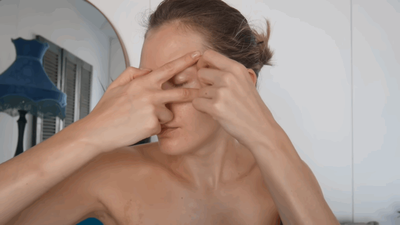 Woman performing facial lymphatic drainage massage with fingers on her forehead and eye area