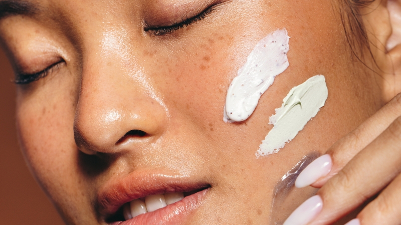 A woman applies two different cruelty-free Korean skincare creams on her cheek