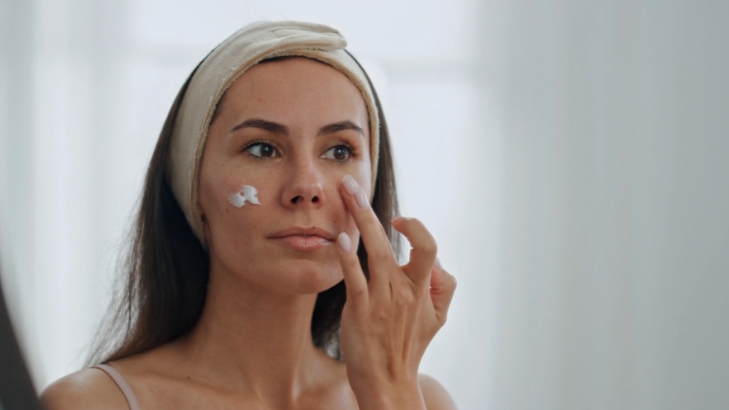 A woman applies moisturizer to her face with her fingers