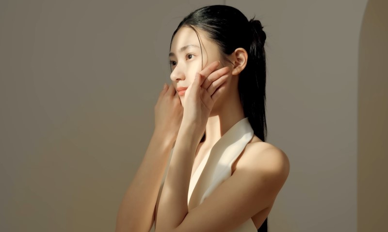A woman with long hair wearing a white top checking her soft skin
