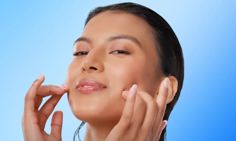 A woman gently touches her face with her hands, highlighting the use of snail mucin in her skincare routine