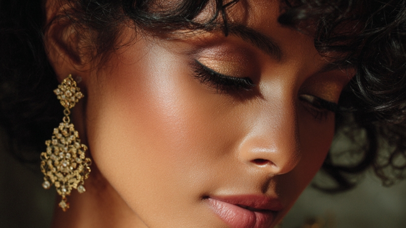 Soft gold eyeshadow and ornate gold earrings create a balanced, polished look on the model’s face