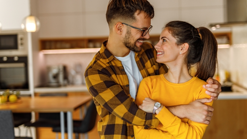 Couple wearing matching yellow tones smiling at each other in a warm kitchen setting