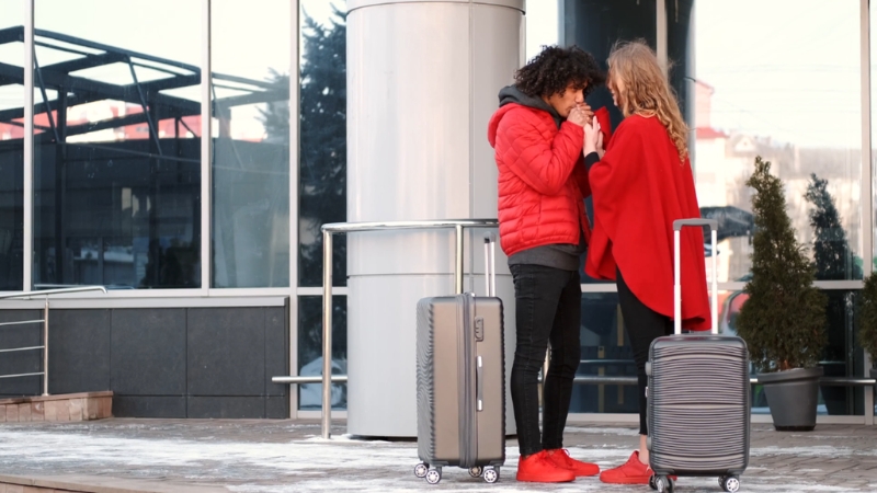 Couple in matching red outerwear standing together with luggage outside a modern building