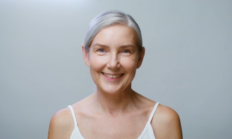 Close-up portrait of an older adult female showing genuine joy, wearing a simple white camisole