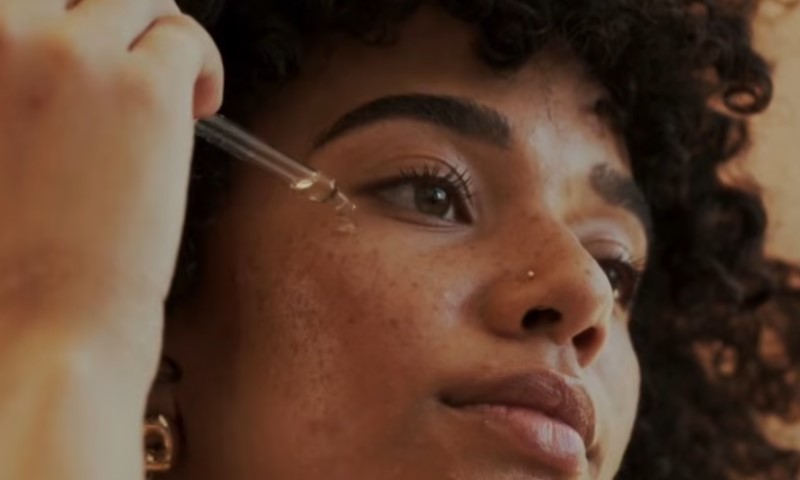 Close-up of dark-skinned woman applying serum near her eye with a dropper