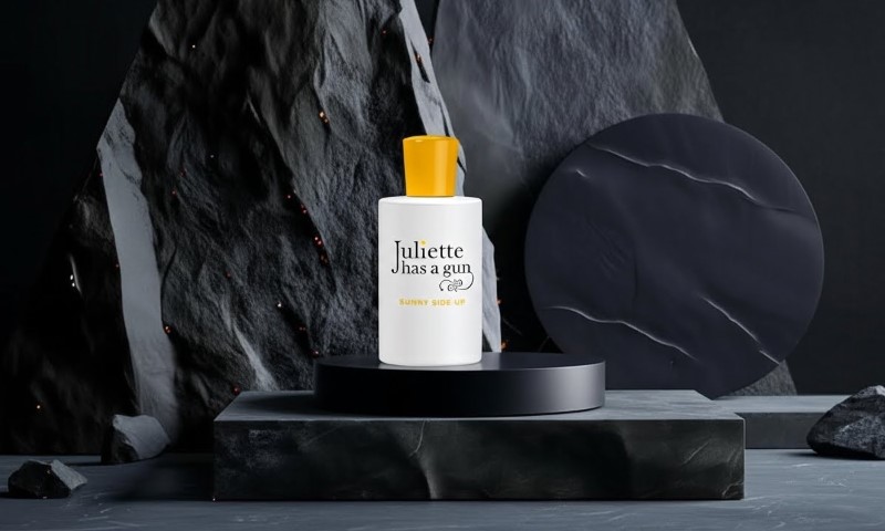 Juliette Has a Gun Sunny Side Up perfume bottle resting on a dark marble pedestal against a dramatic, textured black rock backdrop
