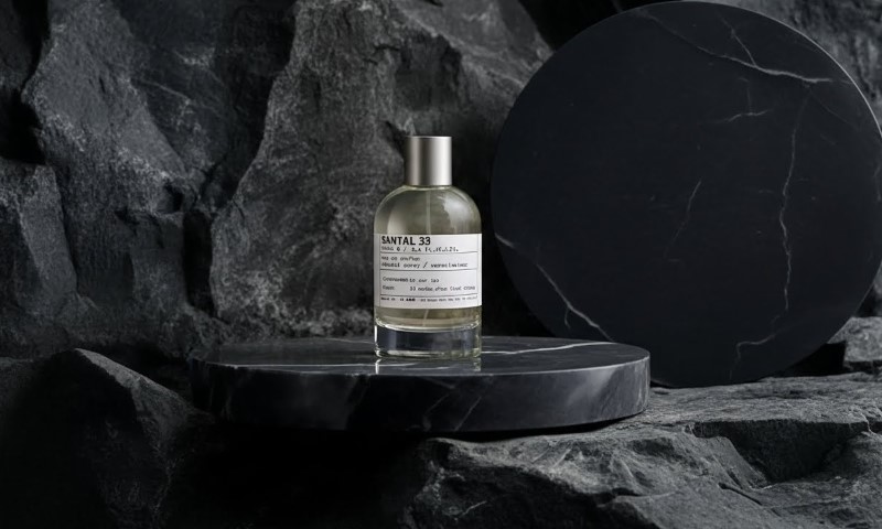 Santal 33 perfume bottle resting on a dark marble pedestal against a dramatic, textured black rock backdrop