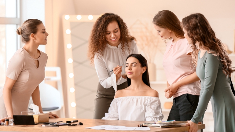 A makeup artist doing makeup on a client while a group of women watch in the studio