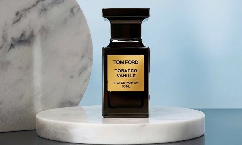 Tobacco Vanille Eau de Parfum fragrance bottle on a white marble pedestal against a bright blue background