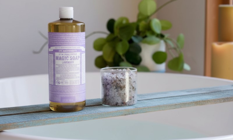 A bottle of Dr. Bronner's lavender soap and a glass candle holder with lavender salts sit on a wooden surface