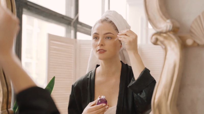 Woman applying facial serum in mirror as part of skincare routine