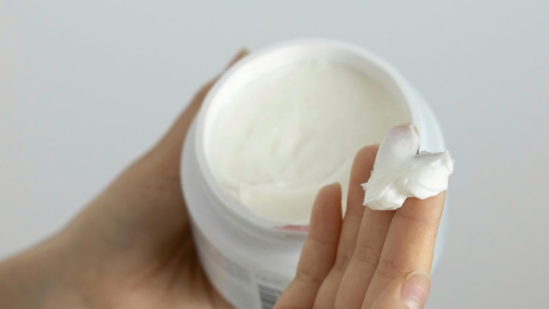 Hand holding a small amount of cream taken from a skincare jar for patch testing
