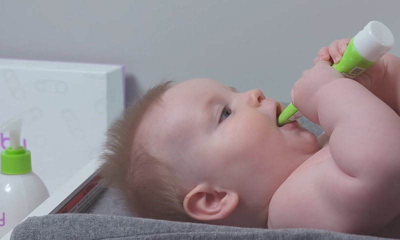 Baby lying on a changing table, holding a green tube with both hands
