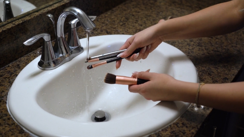 Person washing makeup brushes in a sink to support better skin hygiene