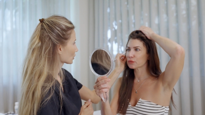 Woman examining her face in a mirror during a cosmetic consultation with a clinician