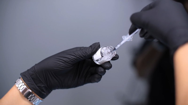 Close-up of gloved hands drawing dermal filler into a syringe for cosmetic injectable treatment