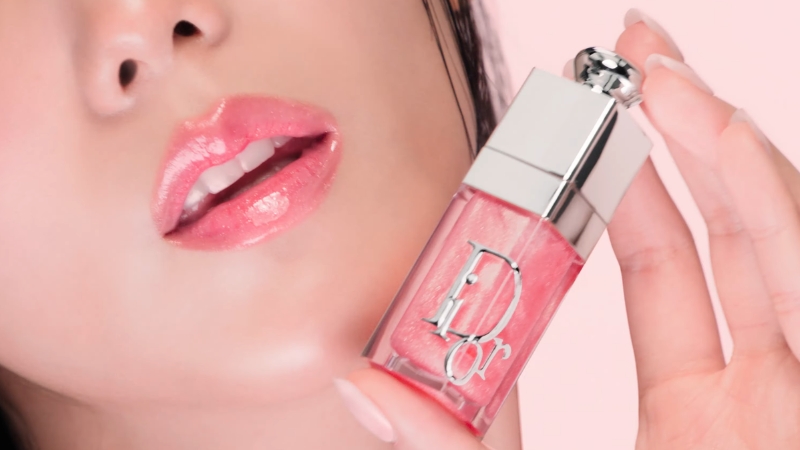 Close-up of glossy pink lip product held near lips as a Women’s Day beauty gift idea