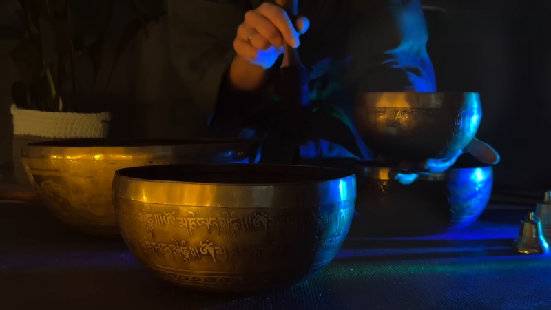 Practitioner plays Tibetan singing bowls during a sound healing session in a dimly lit room