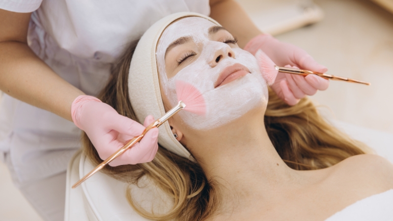 Esthetician applying a facial mask treatment to a client during a professional skincare session