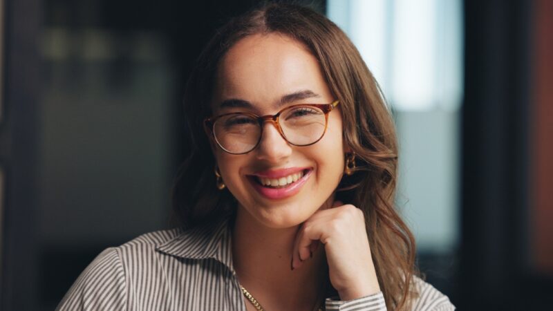 A smiling woman wears tortoiseshell glasses indoors