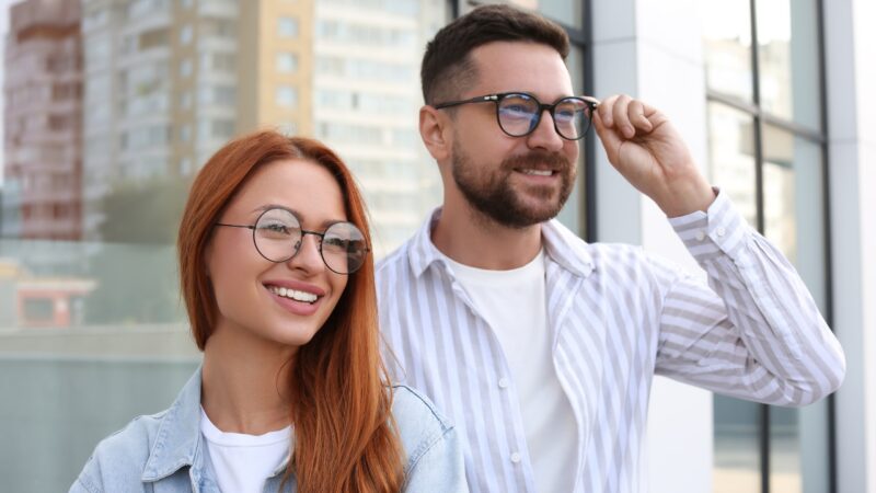 A smiling couple wears stylish glasses outside a modern city building