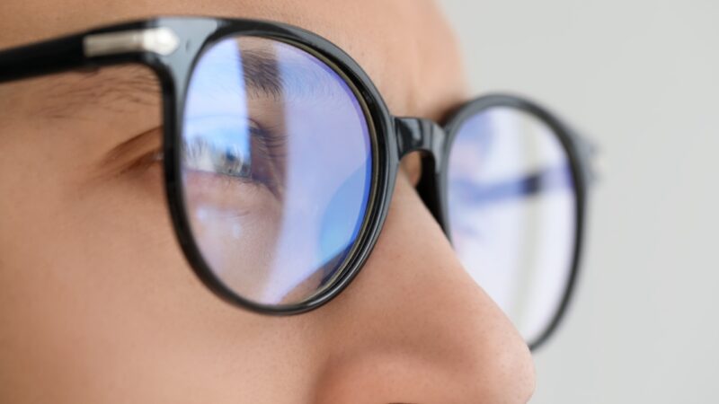 A close-up shows blue light reflections on black glasses lenses