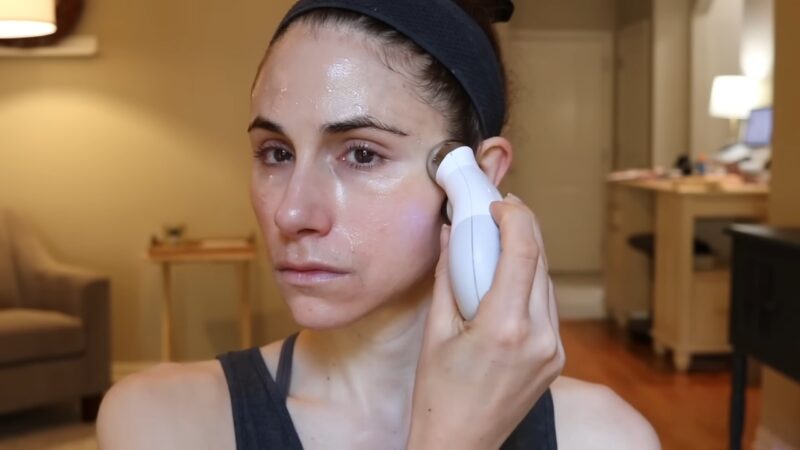 A woman uses a microcurrent device on the side of her face