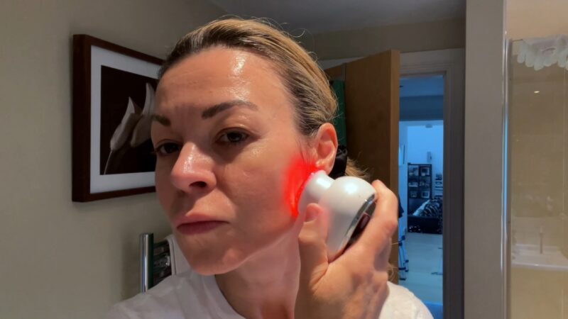A woman uses a light-up microcurrent device along her cheek